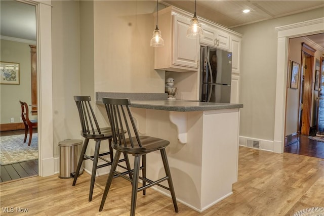 kitchen with stainless steel refrigerator, a kitchen breakfast bar, decorative light fixtures, white cabinets, and ornamental molding