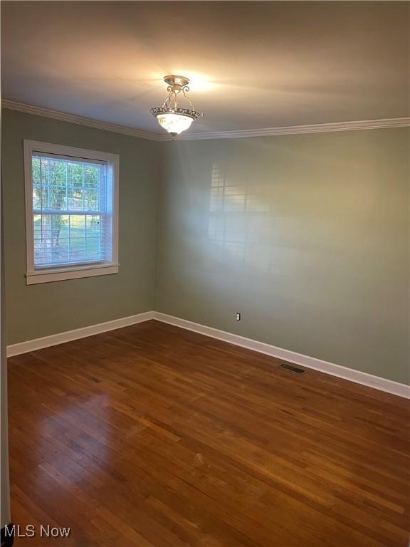 empty room with crown molding and dark wood-type flooring