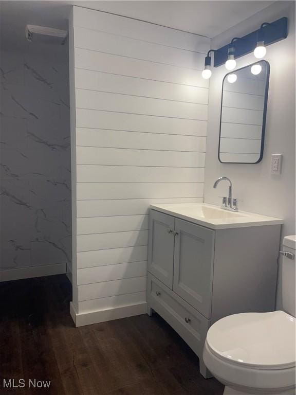 bathroom featuring wooden walls, vanity, wood-type flooring, and toilet