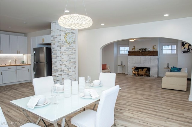 dining room featuring ceiling fan with notable chandelier, light wood-type flooring, and a fireplace