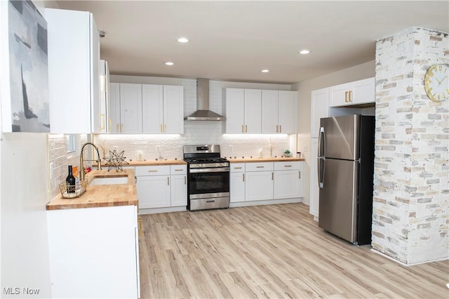 kitchen with butcher block counters, white cabinetry, sink, wall chimney range hood, and appliances with stainless steel finishes