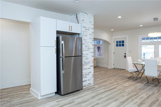 kitchen with white cabinets, decorative light fixtures, stainless steel fridge, and light hardwood / wood-style flooring