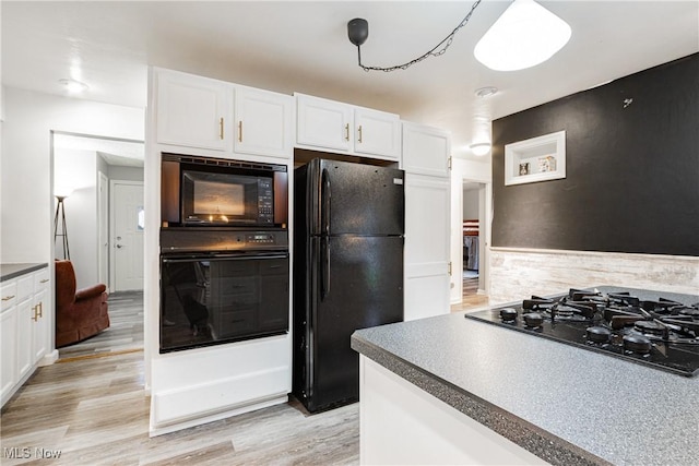 kitchen featuring pendant lighting, white cabinets, black appliances, and light hardwood / wood-style floors