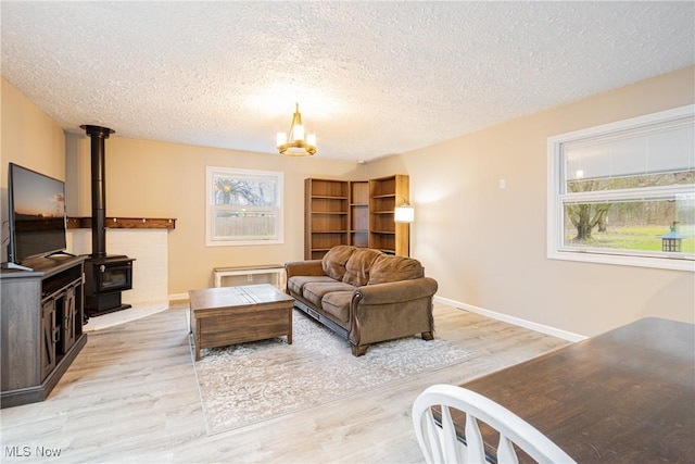 living room featuring a wood stove, light hardwood / wood-style floors, a textured ceiling, and an inviting chandelier