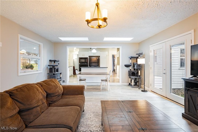 living room featuring french doors, a textured ceiling, a skylight, and light hardwood / wood-style floors