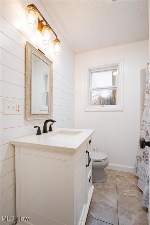 bathroom with wooden walls, vanity, a textured ceiling, and toilet