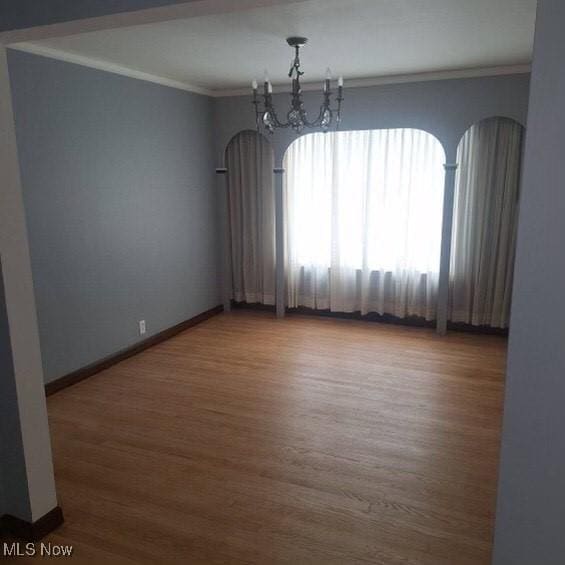 empty room featuring hardwood / wood-style floors, crown molding, and a notable chandelier