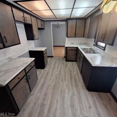 kitchen with light stone countertops, sink, dark brown cabinets, and light wood-type flooring