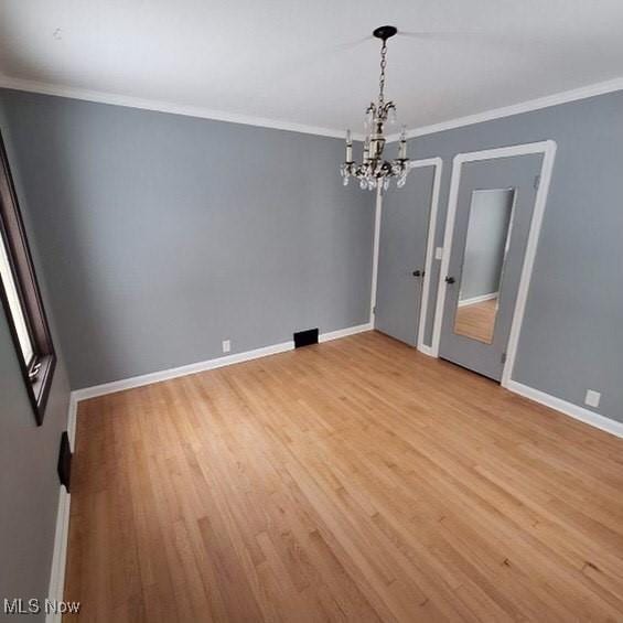 spare room featuring a chandelier, light wood-type flooring, and ornamental molding