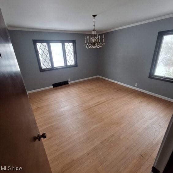 empty room with ornamental molding, plenty of natural light, a chandelier, and light wood-type flooring