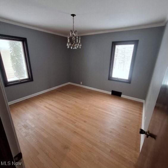 spare room with an inviting chandelier, ornamental molding, and light wood-type flooring