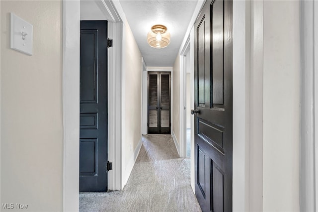 hall with light colored carpet and a textured ceiling