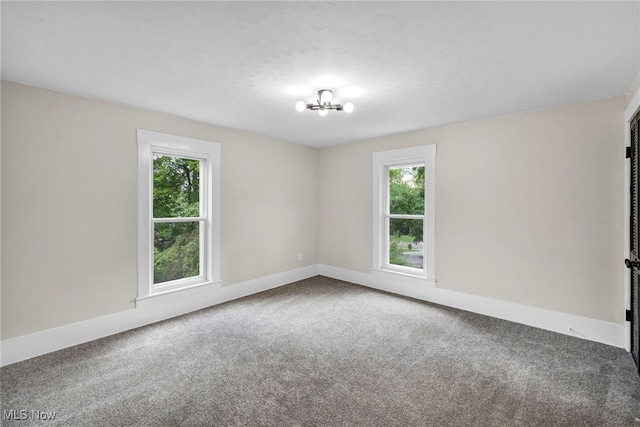 carpeted spare room featuring a healthy amount of sunlight and a notable chandelier