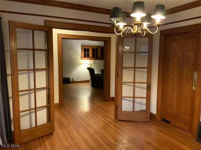 unfurnished dining area with a chandelier, hardwood / wood-style floors, french doors, and crown molding