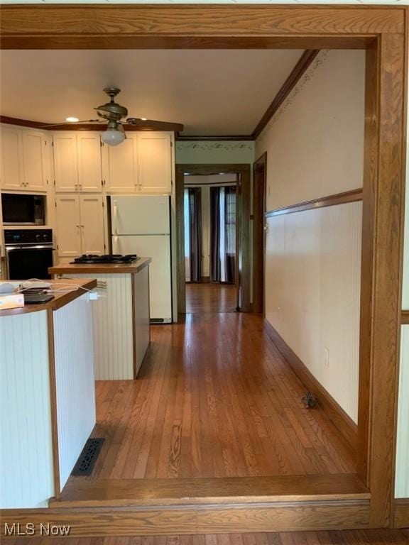 kitchen with black appliances, white cabinets, crown molding, ceiling fan, and dark hardwood / wood-style floors