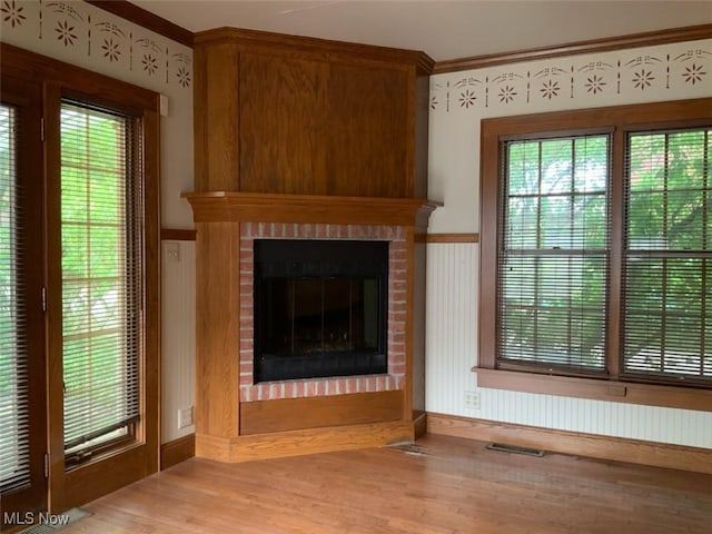 unfurnished living room featuring a wealth of natural light, light wood-type flooring, and a brick fireplace