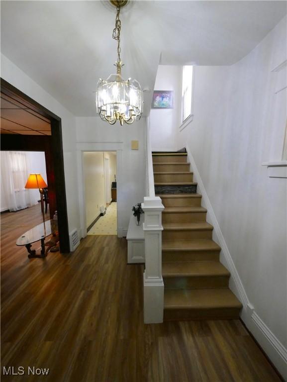 stairs featuring wood-type flooring and an inviting chandelier