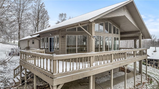 snow covered back of property featuring a sunroom and a wooden deck