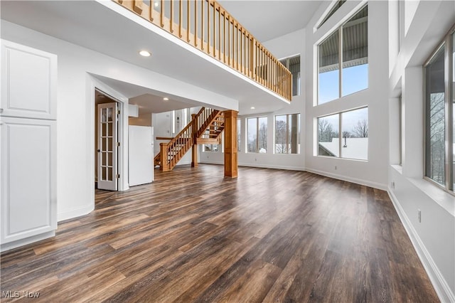 unfurnished living room featuring a towering ceiling and dark hardwood / wood-style floors