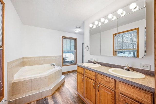 bathroom with tiled bath, a wealth of natural light, vanity, and wood-type flooring