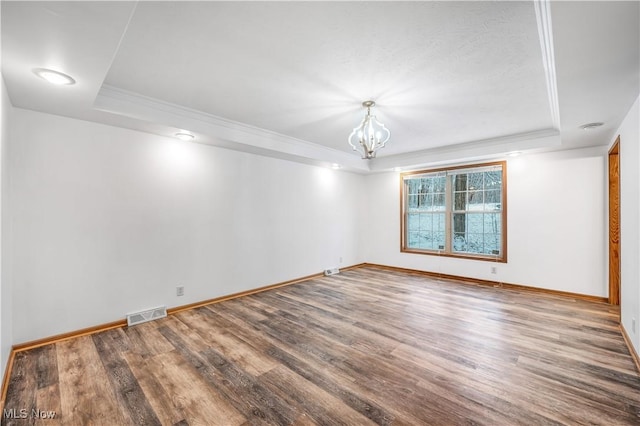 spare room with a tray ceiling, hardwood / wood-style floors, ornamental molding, and an inviting chandelier