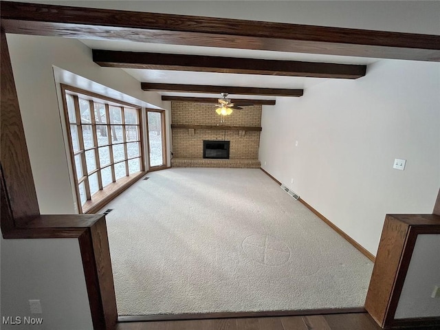 unfurnished living room featuring ceiling fan, a fireplace, carpet floors, and beam ceiling