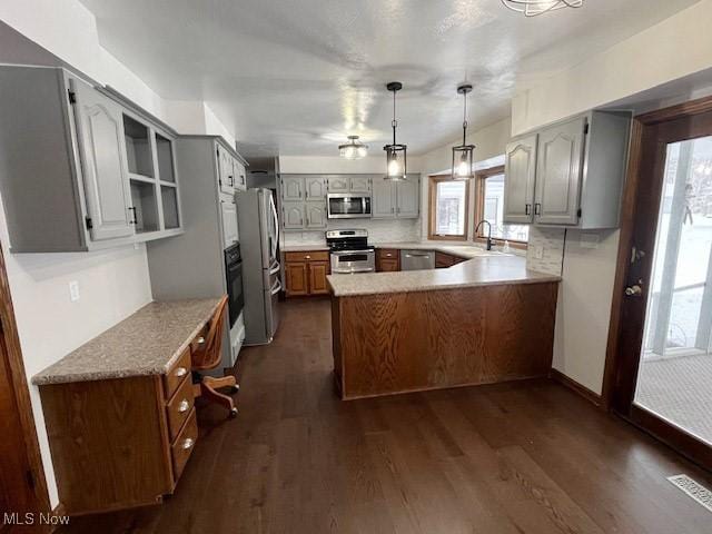 kitchen featuring appliances with stainless steel finishes, sink, gray cabinetry, hanging light fixtures, and dark wood-type flooring