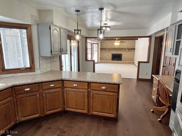 kitchen featuring tasteful backsplash, hanging light fixtures, kitchen peninsula, a brick fireplace, and dark wood-type flooring