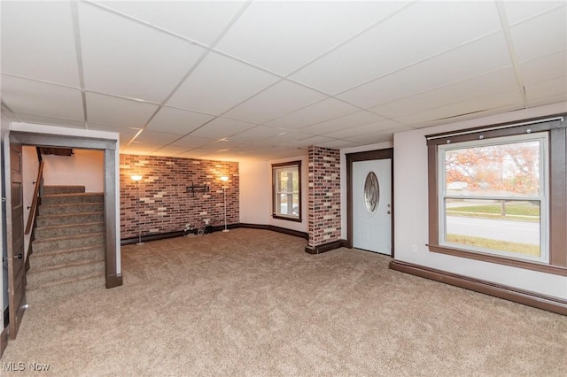 basement featuring a paneled ceiling, carpet floors, and brick wall