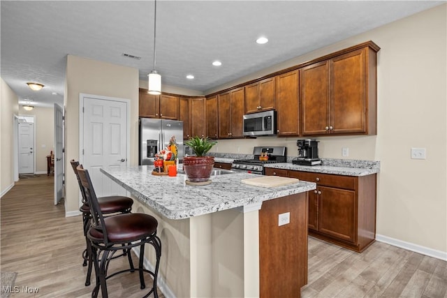 kitchen with a breakfast bar, light hardwood / wood-style floors, appliances with stainless steel finishes, decorative light fixtures, and a kitchen island