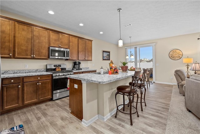 kitchen featuring pendant lighting, a center island with sink, light stone counters, appliances with stainless steel finishes, and a kitchen bar