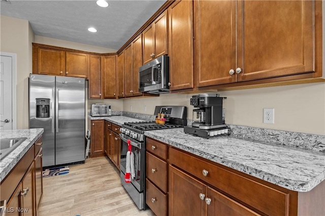 kitchen with light stone countertops, sink, stainless steel appliances, and light hardwood / wood-style floors