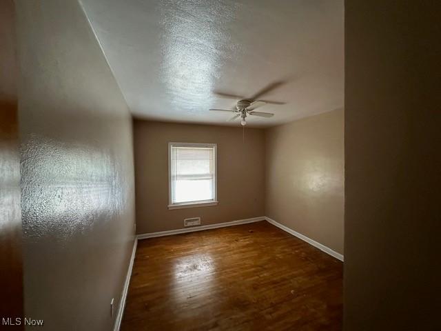 empty room featuring ceiling fan, dark hardwood / wood-style flooring, and a textured ceiling