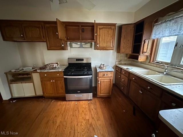 kitchen with backsplash, stainless steel range with gas cooktop, sink, light wood-type flooring, and range hood