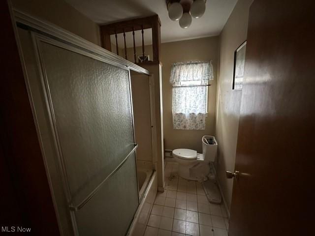 bathroom featuring tile patterned flooring, bath / shower combo with glass door, and toilet