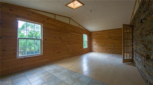 empty room with a textured ceiling, lofted ceiling with skylight, and wood walls