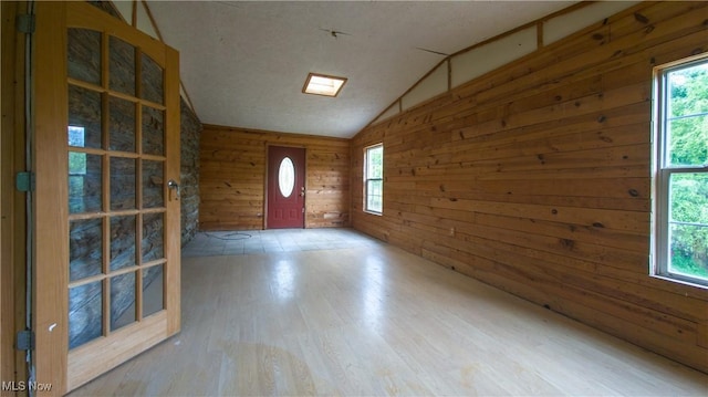 foyer entrance with hardwood / wood-style floors, vaulted ceiling, a healthy amount of sunlight, and wood walls