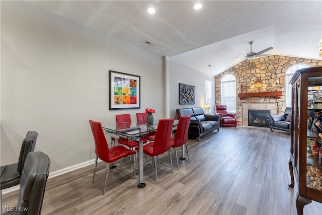 dining room with a stone fireplace, ceiling fan, vaulted ceiling, and hardwood / wood-style flooring