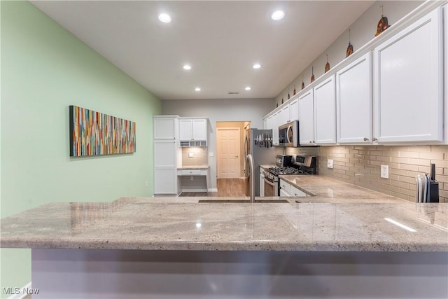 kitchen with kitchen peninsula, appliances with stainless steel finishes, backsplash, light stone counters, and white cabinets