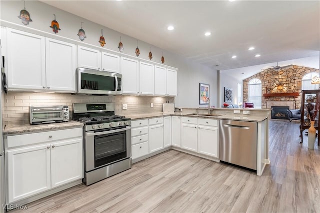 kitchen with white cabinets, sink, a fireplace, appliances with stainless steel finishes, and kitchen peninsula