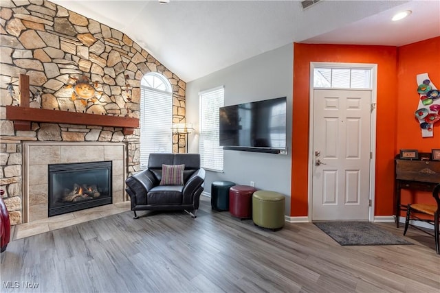 living room featuring wood-type flooring, vaulted ceiling, and a stone fireplace