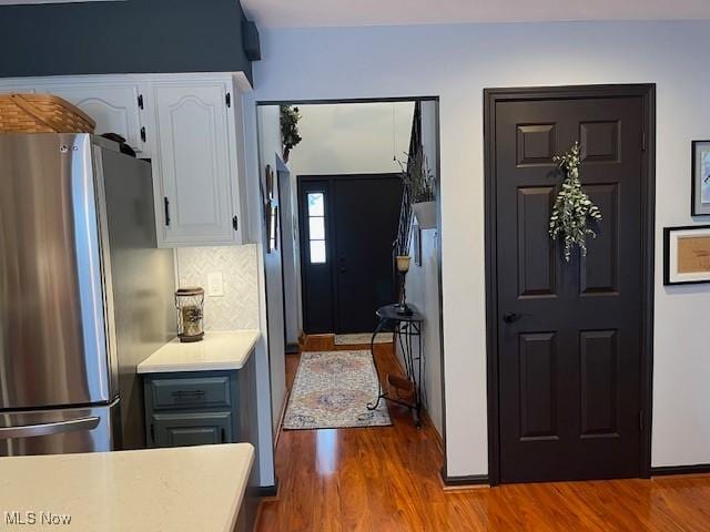 kitchen with hardwood / wood-style flooring, white cabinets, stainless steel refrigerator, and decorative backsplash