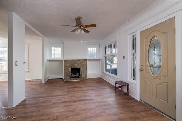 foyer entrance featuring ornamental molding, a textured ceiling, ceiling fan, dark hardwood / wood-style floors, and a stone fireplace