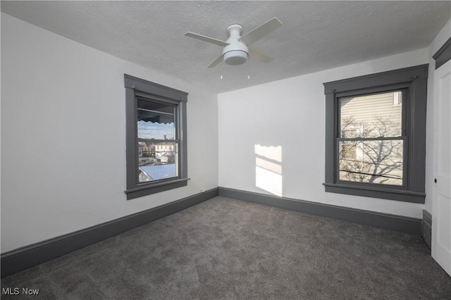 unfurnished room with ceiling fan, dark carpet, and a textured ceiling