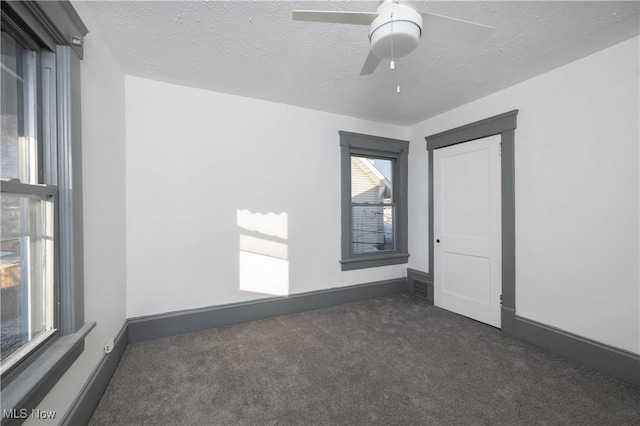 empty room with dark colored carpet, ceiling fan, and a textured ceiling