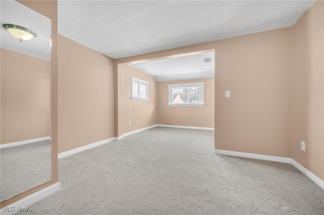 unfurnished room with carpet flooring, visible vents, baseboards, and a textured ceiling