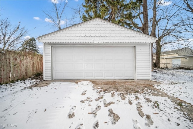 snow covered garage featuring a garage and fence