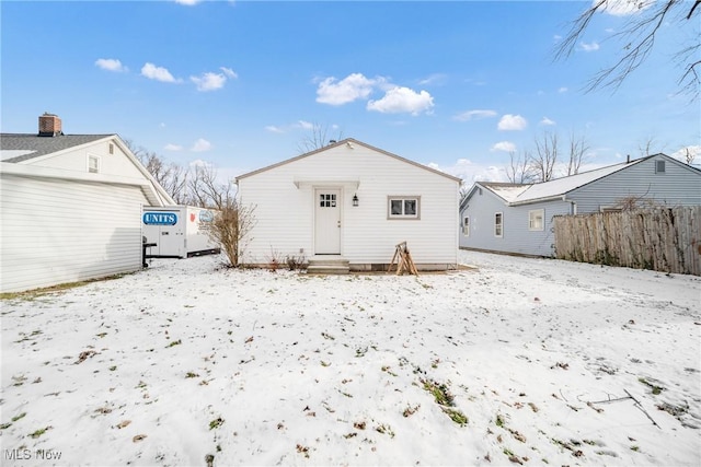 snow covered back of property with a detached garage and fence