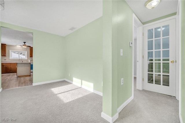 unfurnished living room featuring visible vents, baseboards, a sink, ceiling fan, and light carpet