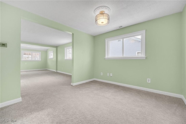 empty room featuring visible vents, carpet floors, a textured ceiling, and baseboards